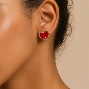 Close-up detail of a red enamel heart stud earring with zircon accent on model's ear