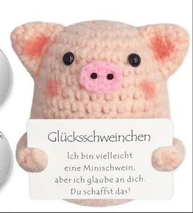 Close-up of pink crocheted piglet holding an encouraging German gift message card