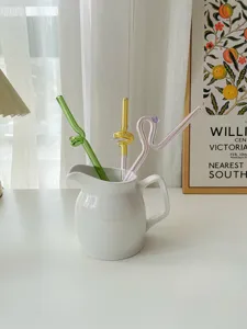 Colorful glass drinking straws in a white ceramic pitcher, aesthetic tabletop detail view.