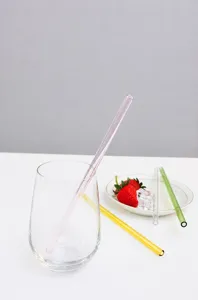 Close-up of colorful glass drinking straws set in a clear glass with a strawberry plate.