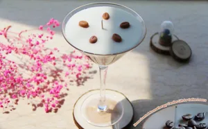 Close-up of scented candle in martini glass with coffee beans on wooden table with pink flowers.