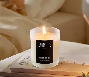 Scented soy wax candle in frosted glass jar with warm burning flame for cozy home decor.