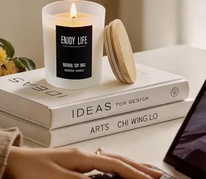 Frosted glass scented soy candle detail shot with wooden lid on aesthetic decor books.