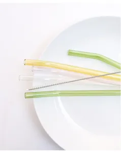 Detailed view of colorful glass straws set with cleaning brush on white plate showcase.