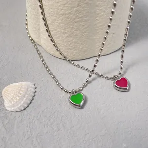 Nahaufnahme von minimalistischen Herz-Emaille-Anhängern in Grün und Pink an Silberketten.