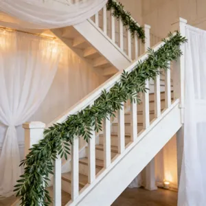 Lush artificial olive leaf garland draped on white stairs for indoor wedding decor