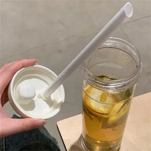Detailed view of transparent plastic straw cup with white lid and straw, filled with lemon water.