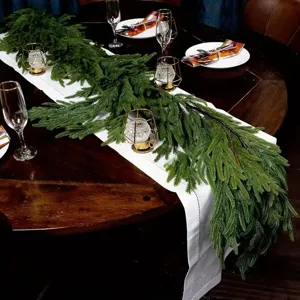 Realistic Norfolk pine garland decorating a dark wood dining table for Christmas.