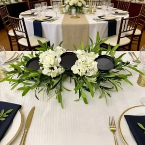 Detail view of artificial olive leaf and white flower floral centerpiece with 3 candle holders