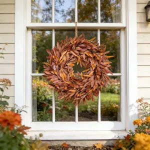 Detailed view of an autumn wreath with orange leaves and berries on a white window.