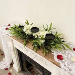 Artificial olive leaf centerpiece with three black candle holders on a vintage mantle