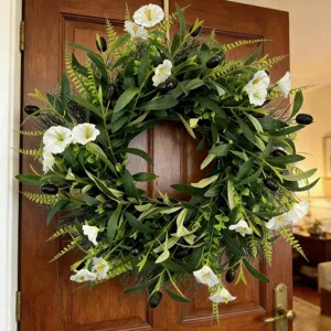 Close-up of artificial olive wreath with white flowers displayed on a wooden door
