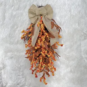 Detail of autumn teardrop wreath with orange berries and a large burlap bow hanging