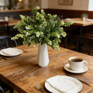 Lush artificial eucalyptus and olive branches in a white vase on a rustic table.