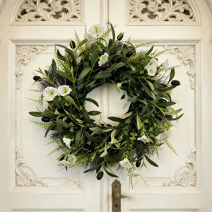Olive wreath with white flowers and dark olives hanging on an ornate white door.