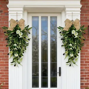 Symmetric olive teardrop wreaths with burlap bows and white flowers on a white door