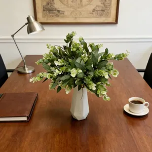 Detailed view of artificial eucalyptus and olive greenery in a white vase on desk