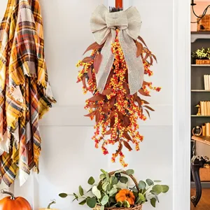 Rustic autumn teardrop wreath featuring orange berries and burlap bow hanging on a white door