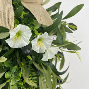 Close-up detail of artificial olive wreath featuring white petunias and burlap bow