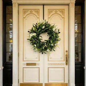 Elegant artificial olive leaf wreath with white flowers hanging on a classic cream door