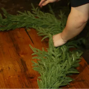 Detail shot of a hand touching the realistic texture of PE Norfolk pine Christmas garland.