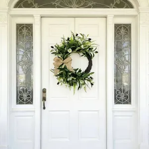 Artificial olive wreath with white flowers and burlap bow hanging on a white front door.