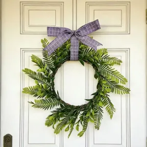 Close-up of an artificial Persian leaf wreath with a purple bow on a white door