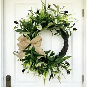 Beautiful artificial olive wreath with a burlap bow and flowers on a white door
