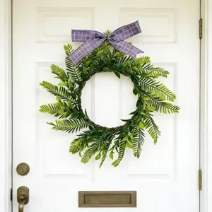 Detail of artificial green Persian leaf wreath with purple plaid bow on white door.