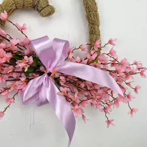 Close-up of heart-shaped artificial wreath with pink blossoms and purple ribbon.