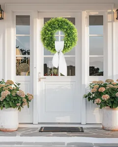 Lush artificial boxwood wreath with white bow hanging on a modern white front door