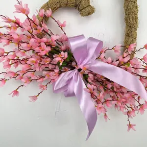 Detailed macro view of pink artificial flowers and purple bow on a heart-shaped wreath.