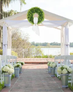 Outdoor wedding scene featuring a green faux boxwood wreath with a white fabric bow.