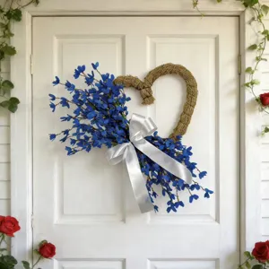 Blue artificial flower heart-shaped wreath with white satin bow hanging on a white door
