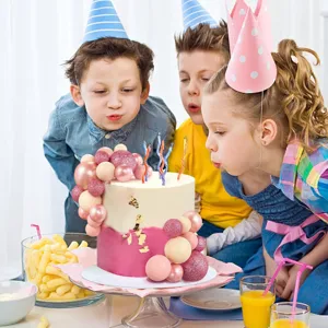 Kids blowing out candles on a birthday cake with elegant pink and beige ball toppers