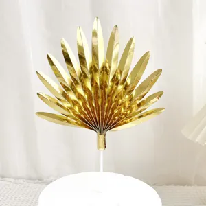 Gold fan-shaped leaf cake topper detail close-up, shiny paper baking decoration for party.