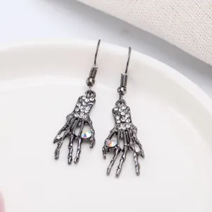 Detalle de pendientes góticos de mano de esqueleto con pedrería iridiscente y metal