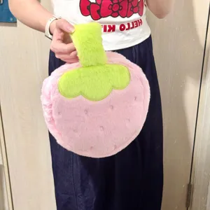 Detail view of a soft pink plush strawberry-shaped cosmetic bag featuring green leaf accents