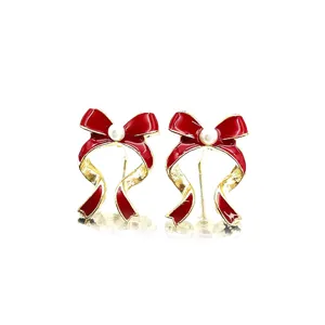 Detailed view of red enamel bow earrings with a central pearl for Christmas outfits.