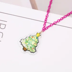 Gros plan d'un collier rose avec un pendentif sapin de Noël rempli de paillettes.