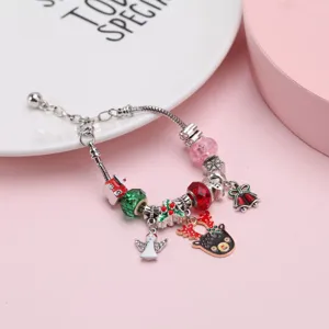 Detalle de pulsera navideña DIY con colgantes de reno y ángel sobre un fondo rosa suave