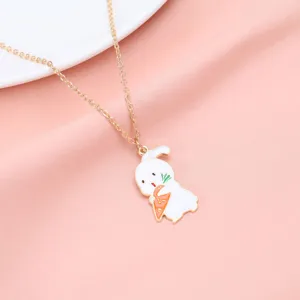 Cute white rabbit pendant necklace with carrot detail on pink fabric background.