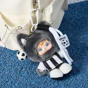 Adorable llavero de peluche de fútbol con sudadera gris y camiseta a rayas colgado en una mochila