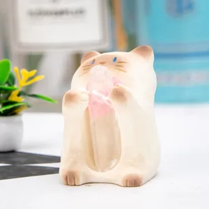 Close-up of a cute cream cat figurine holding a natural pink crystal stone for desk decor