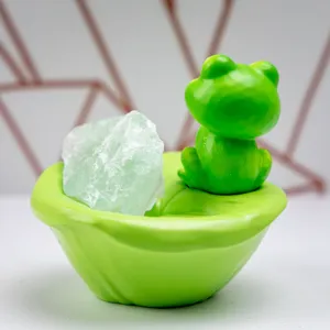 Gros plan d'une figurine de grenouille en résine et cristal vert sur nénuphar.