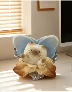Gros plan d'une figurine de chat en céramique avec ailes bleues et socle feuille.