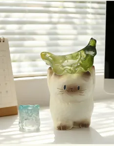 Vue détaillée d'une adorable figurine de chat siamois avec une feuille sur un bureau ensoleillé.