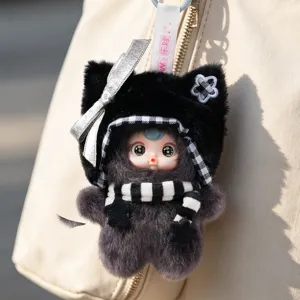 Adorable plush monster doll keychain with cat-ear hood and striped scarf on a beige bag