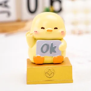 Macro detail view of a cute yellow cartoon chicken resin figurine holding an 'Ok' sign on gold base