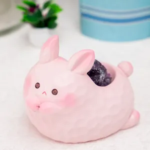 Gros plan d'une figurine de lapin rose en résine tenant un cristal d'améthyste violet